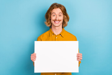 Portrait of attractive cheerful long-haired guy holding in hands copy space banner isolated over bright blue color background