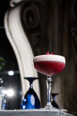 Pink Clover Club Cocktail in Coupe Glass with Layer of Foam and flower Garnish isolated on dark Background