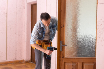 Young handyman in uniform changing door lock