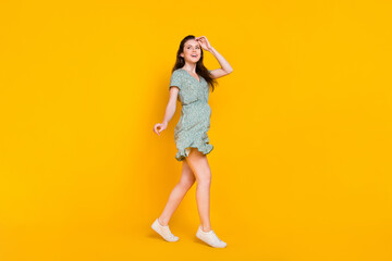 Fototapeta na wymiar Photo of dreamy excited woman wear print dress dancing running looking empty space isolated yellow color background