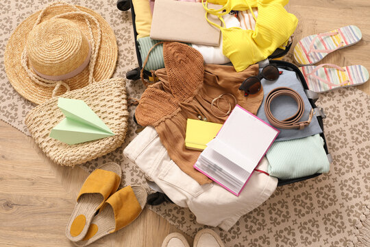 Open suitcase with clothes, shoes and summer accessories on wooden floor, top view