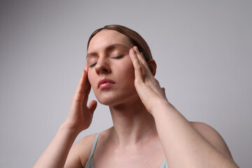 Middle aged woman touches her face doing a lift massage posing on white wall.