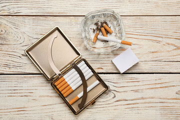 Cigarettes in case, matchbox and ashtray with stubs on white wooden table, flat lay