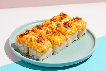 Hot sushi roll with cream cheese top and crispy onion. Baked sushi with salmon, cream cheese topped. Hot maki sushi  on coloured background in minimal style.