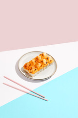 Hot maki roll with cheese on coloured background. Baked sushi roll with salmon inside, rice outside, cheese topped. Maki sushi in minimal style. Japanese menu concept.
