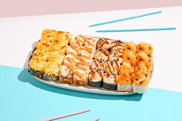Set of hot maki rolls on coloured background. Baked sushi roll assortment on ceramic plate. Maki sushi in minimal style. Japanese menu concept.
