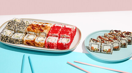 Sushi set on ceramic dishware with coloured chopsticks. Trendy set of maki sushi in minimal style. Modern japanese menu concept. Maki sushi assorted on coloured background.