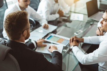 A group of company employees sits at a table in a meeting room. A team of young businessmen working and communicating together in an office. Corporate business team and manager in a meeting