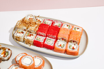Sushi set: Philadelphia, california, canada maki rolls on ceramic plate. Trendy set of maki sushi in minimal style. Modern japanese menu concept. Maki sushi assorted on coloured background.