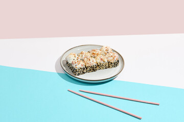 Baked Maki roll with bacon on ceramic plate. Hot sushi roll with sesame outside, bacon and cheese topped on coloured background. Japanese menu concept. Hot maki sushi in modern style.