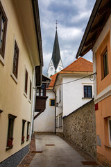Fototapeta na wymiar Narrow street with old houses and tower of church in alpine town Radovljica, Slovenia