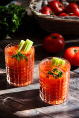 Bloody Mary cocktail, iced tomatoe juice with celery and parsley. Red cocktail on wooden table on a...