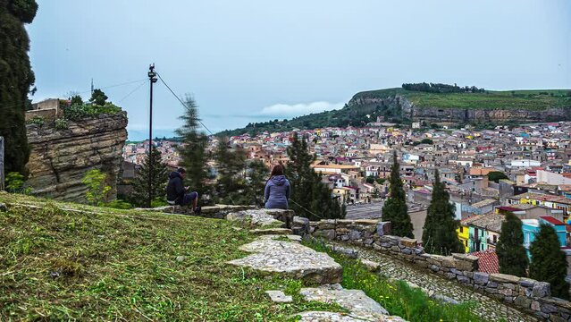 Time lapse shot showing person sitting on rock and watching cityscape of Corleone on Sicily
