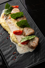 Baked meat and mashed potatoes as a garnish in white plate. Macro close-up on a black background. Delicious meal, restaurant menu concept.