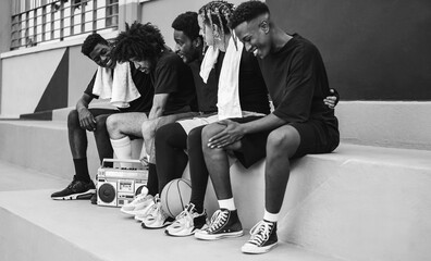 Group of young african people listening music from vintage boombox stereo outdoor after basketball match - Focus on with afro hair - Black and white editing