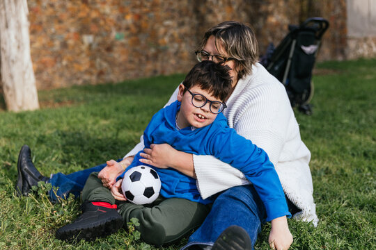 A mom playing with her son who has a disability holding a soccer ball in the park