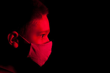 The portrait of a boy wearing in a mask with a red light on the dark background