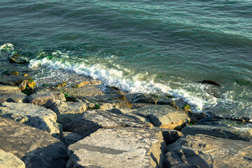 Shiny rocks and crashing waves by the sea with sun glare and seaweed