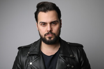 Bearded handsome young man, wearing leather jacket posing on white background.