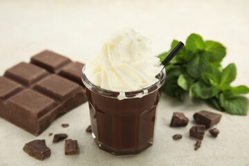 Glass of delicious hot chocolate with whipped cream, chunks and fresh mint on light table