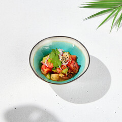 Vegetables salad with tomatoes, cucumbers and onion on white table with hard shadow. Vegan starter in asian style. Summer menu concept. Asian food in minimal design with sun light shadow.