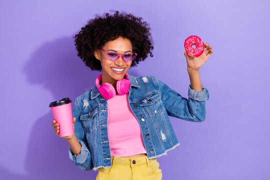 Photo of dreamy funny young woman wear jeans jacket headphones drinking tea eating biscuits isolated violet color background