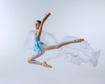 One young girl, aspiring ballerina in blue dress and pointes dancing with cloth isolated on gray background. Art, grace, beauty, ballet school concept