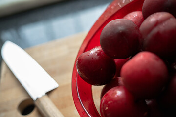 Red plums on bread board with knife and black background