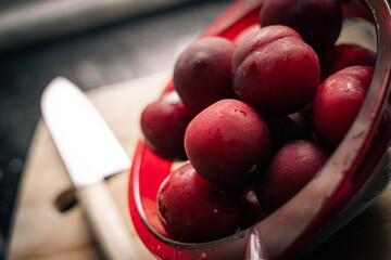 Red plums on bread board with knife and black background