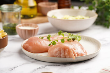 Fresh ingredients for preparing a warm salad on marble surface: chicken breasts, heavy cream, zucchini noodles, italian pasta orecchiette, herbs and sauces