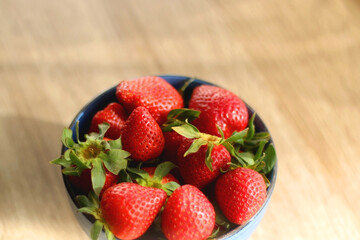 Bowl of fresh strawberries on wooden table, illuminated by sunlight. Selective focus.