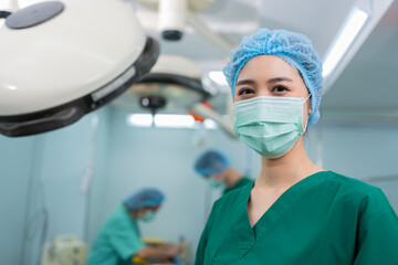 Portrait of Asian woman surgeon with medical mask standing in operation theater at a hospital. Team of Professional surgeons. Healthcare, emergency medical service concept