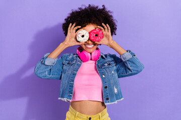 Portrait of beautiful trendy cheery wavy-haired girl holding donuts like glasses isolated over bright violet purple color background