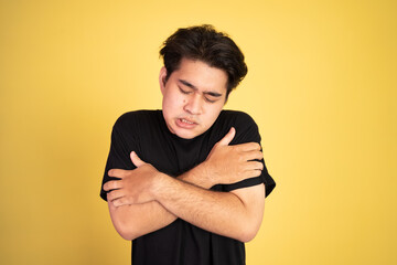 asian young man shivering while holding his two arms hug himself on isolated background