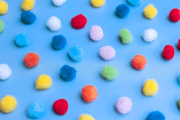 Colorful pom-poms background, bright background, colorful pom-poms scattered in a chaotic manner on a blue background