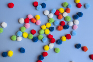 Colorful pom-poms background, bright background, colorful pom-poms scattered in a chaotic manner on a blue background