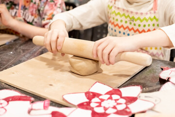 Obraz na płótnie Canvas child potter rolls a brown clay with rolling pin on a special board on a wooden table to make a plate.Pottery workshop.Pottery workshop. teaching schoolchildren. hobbies and leisure for children.