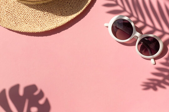Stylish summer vacation concept frame with straw hat, retro sunglasses and tropical leaves shadows on the pink background. Copy space - Powered by Adobe