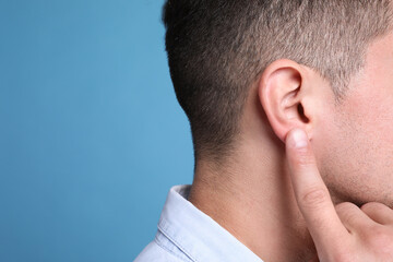 Man pointing at his ear on light blue background, closeup. Space for text - obrazy, fototapety, plakaty