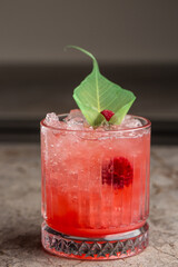 Glass with strawberry mojito cocktail with lemon and mint, cold refreshing drink or beverage with ice on gray background.