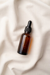top view of amber glass essential oil droppper bottle with pipette on fabric wavy background