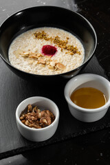 Semolina porridge for breakfast oat with nuts in black bowl served with honey isolated on black stone background. Homemade food. Tasty breakfast.