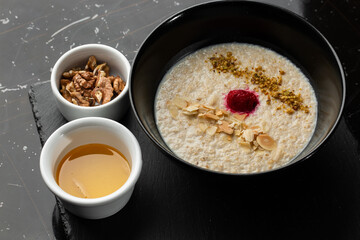 Semolina porridge for breakfast oat with nuts in black bowl served with honey isolated on black stone background. Homemade food. Tasty breakfast.