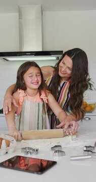 Vertical shot of a Caucasian mother and daughter rolling dough in the kitchen