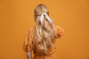 Young woman with stylish bandana on yellow background, back view