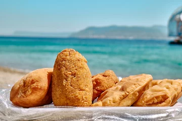 Foto op Canvas Typical Sicilian street food on seaside background. Hot palatable panzerotti (calzone pizza fried in hot oil) and arancina (deep fried rice balls with meat) on paper plate take out. © Caterina Trimarchi