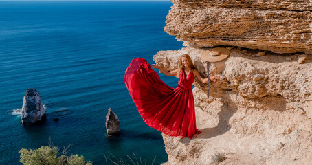 A woman in a red flying dress fluttering in the wind, against the backdrop of the sea.