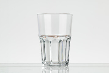 Faceted glass of water, half filled. Translucent glass on a white background.