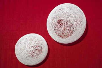 Two decorative white balls, glued from a thread, handmade, for interior decoration, as a vase, on a red textured paper background.