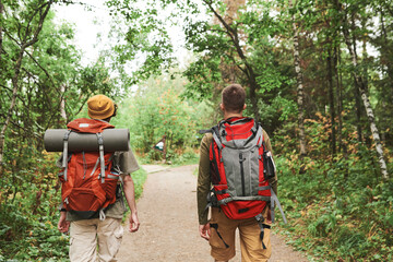Rear view of men with backpacks walking along forest path while hiking together in autumn